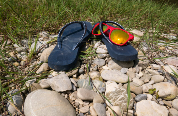 Badesandalen aus Plastik mit einer Sonnenbrille in der sich die Sonne spiegelt